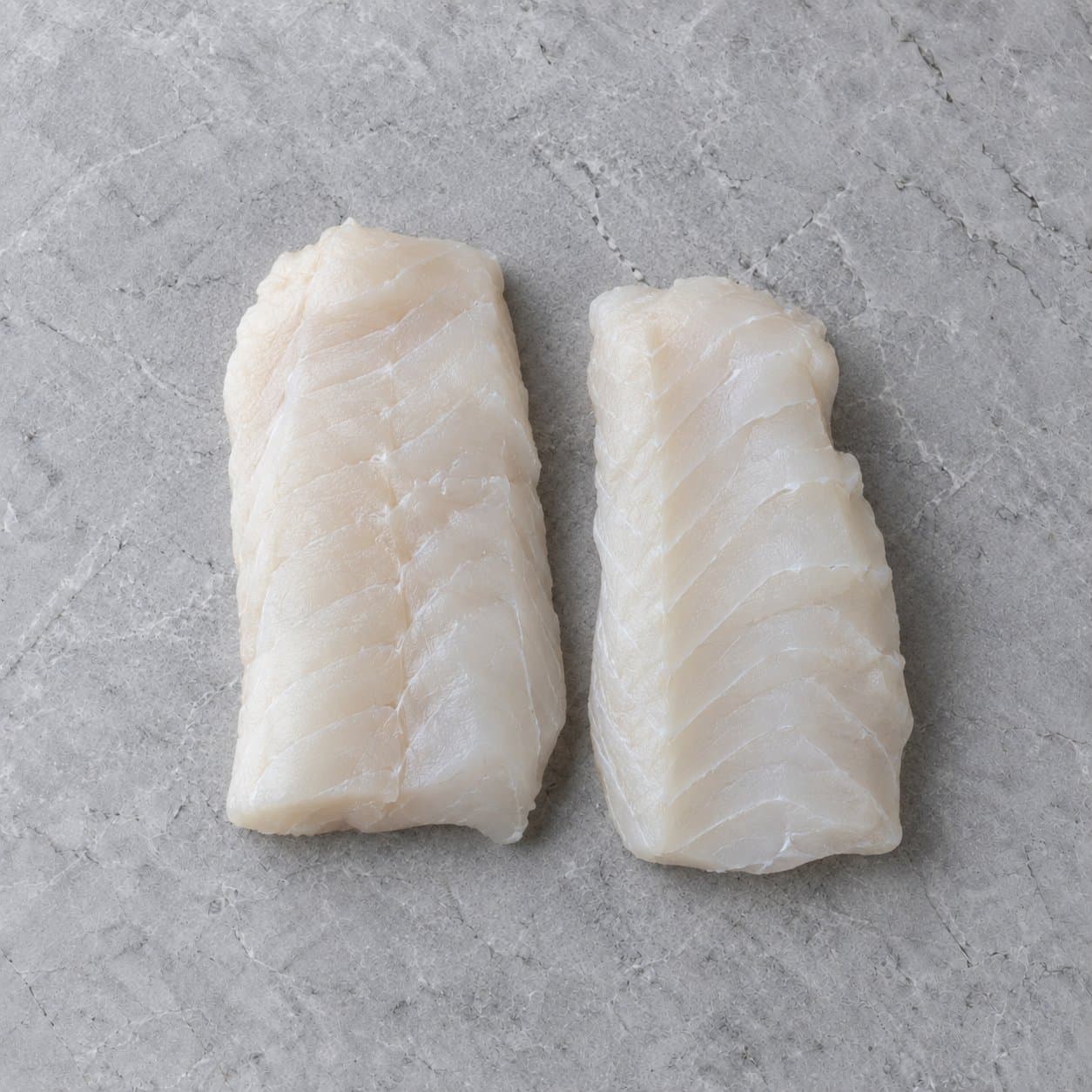 Two thick raw cod loin portions on grey stone
