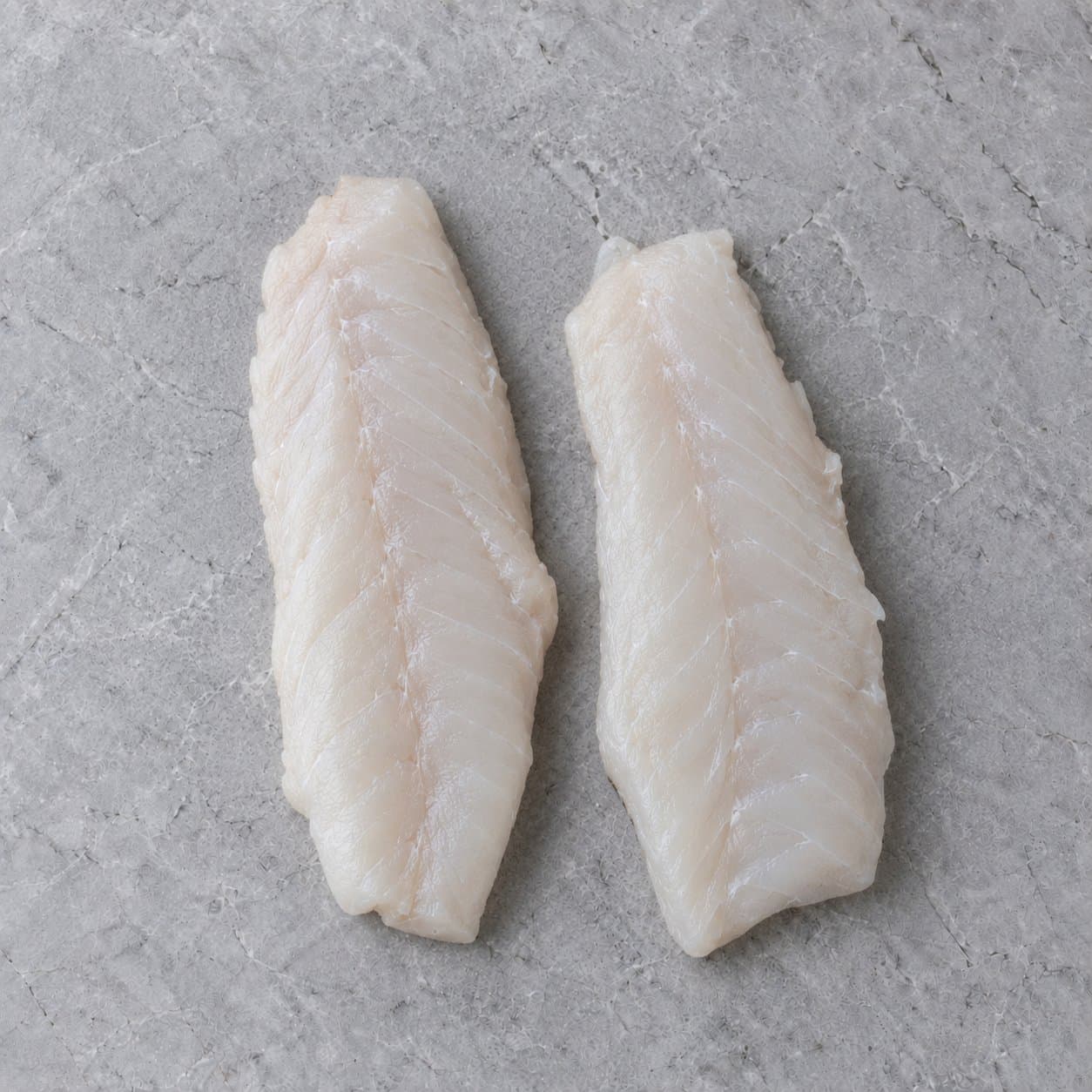 Two raw hake fillets on grey stone