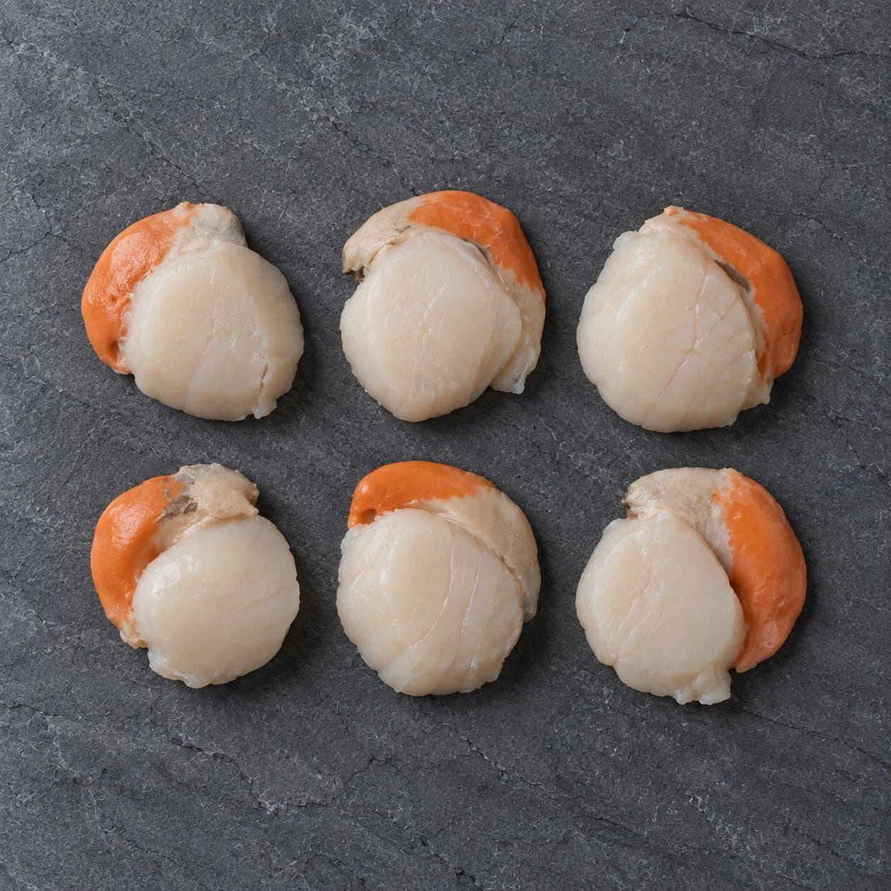 Six raw king scallops with roe on dark slate