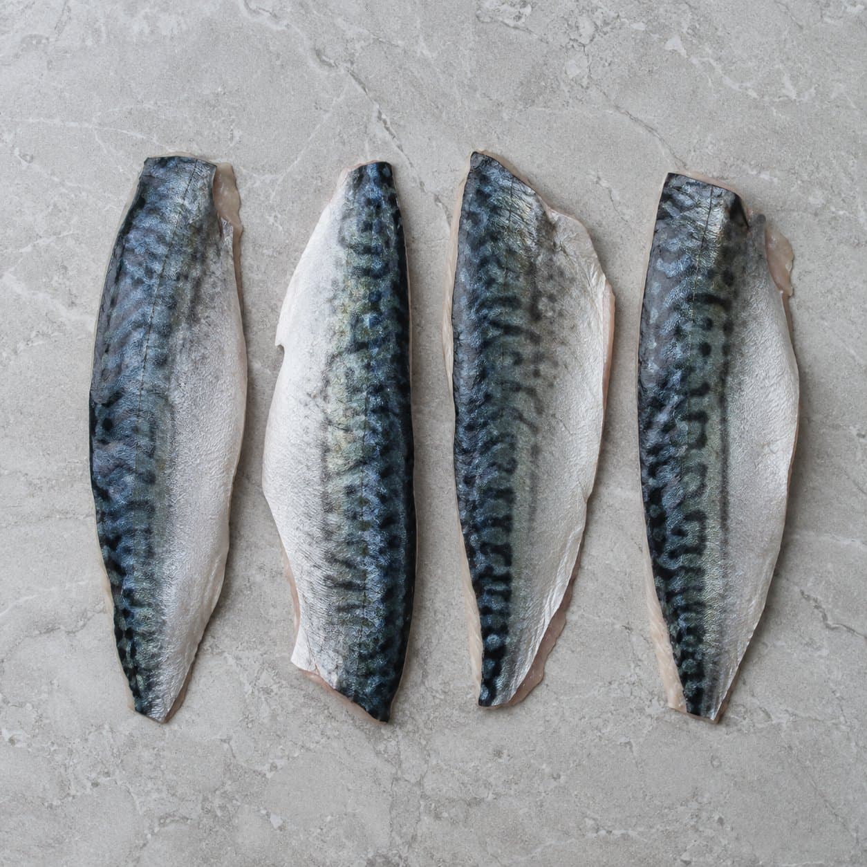 Four raw mackerel fillets, skin side up, on grey stone